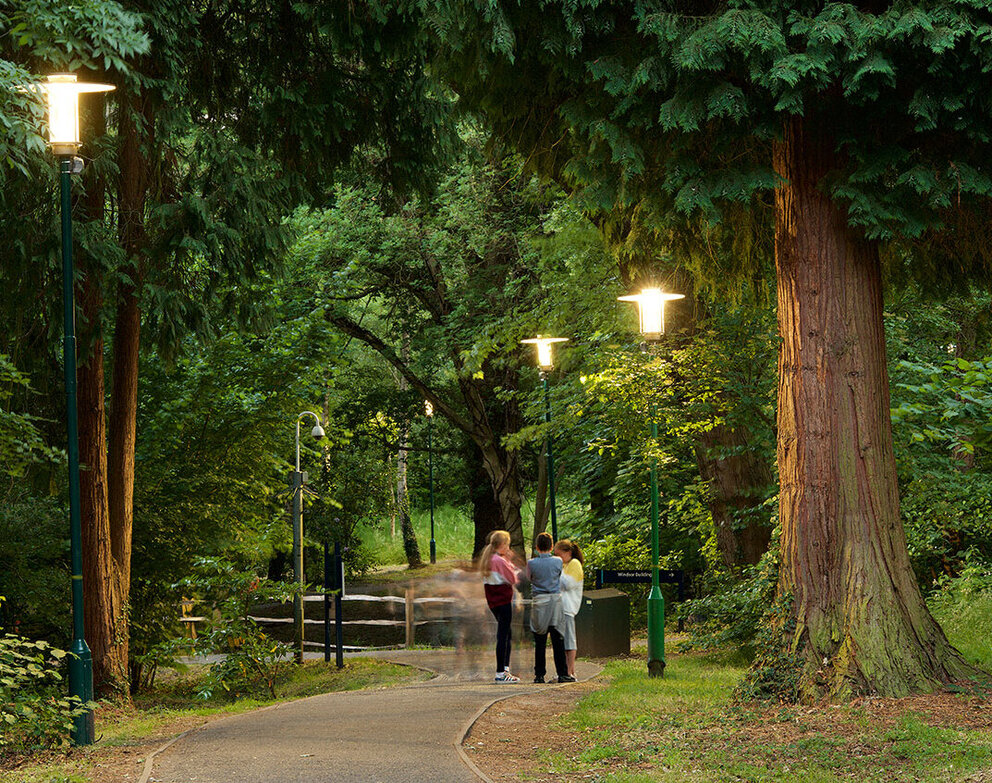 Nachhaltigkeit. Der Kompass unseres Handelns. Personengruppe in einem grünen Park, der von dekorativen SITECO Leuchten beleuchtet wird.